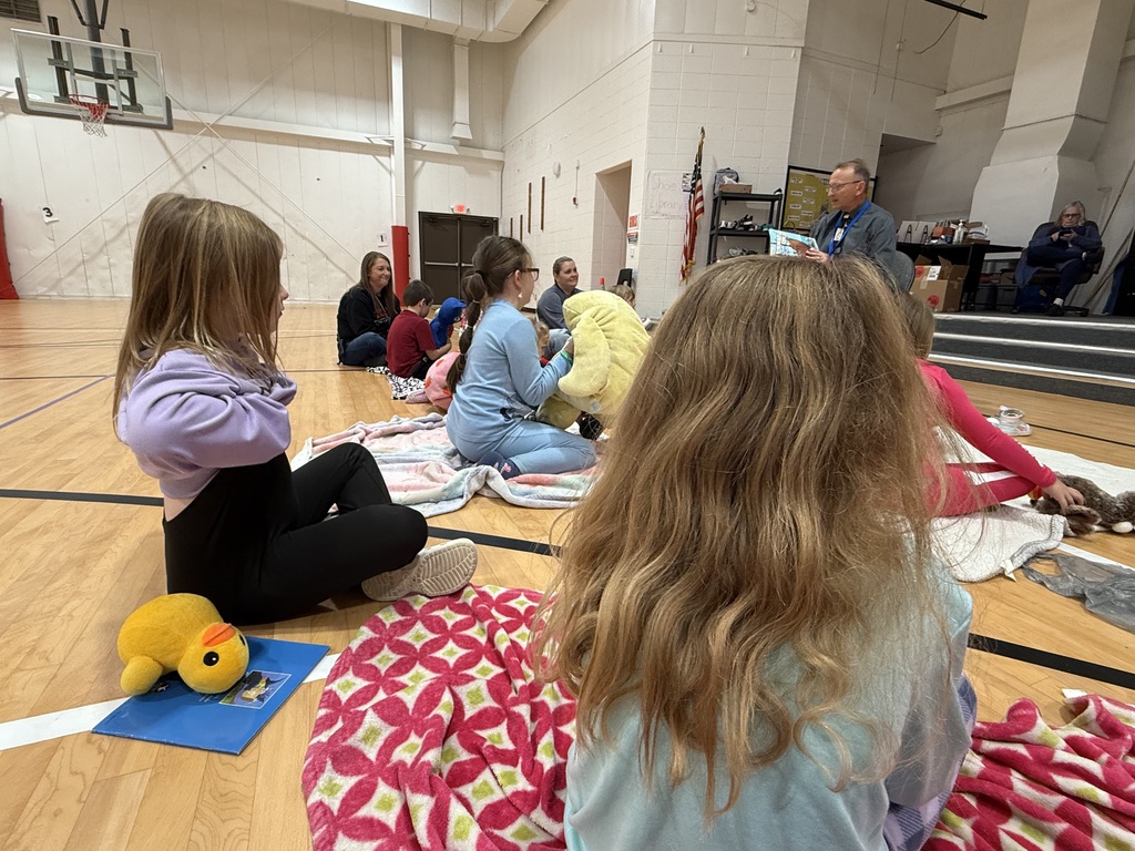 Children sit in a circle on floor, one holds a yellow stuffed animal, another has a blue mat