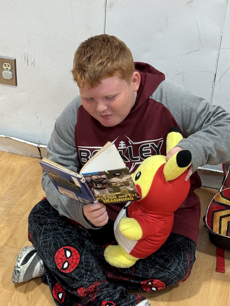 Child sitting on floor with book open, reading, holding a yellow stuffed animal.