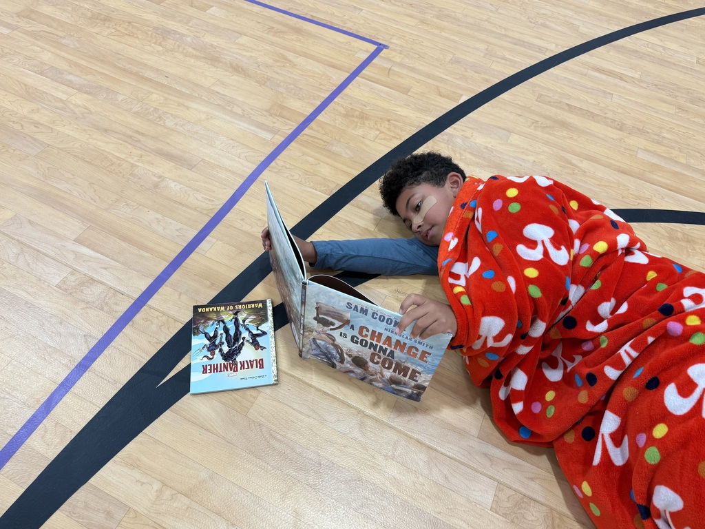 Person lying on floor with books. One book open, another closed next to them. Court floor with painted lines.