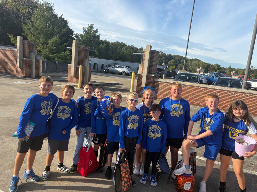 Group of students wearing matching blue shirts pose for a photo outside with bags.
