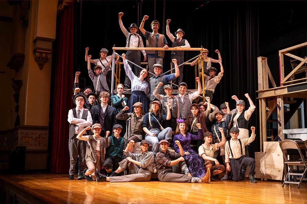 The cast of a musical posing on stage with their fists in the air.