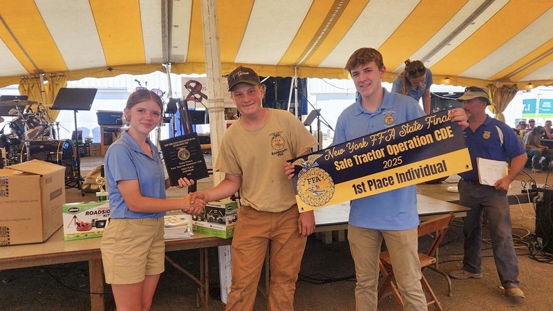 A student with two FFA representatives, one of whom is holding a first place invidividual banner for Safe Tractor Operation.