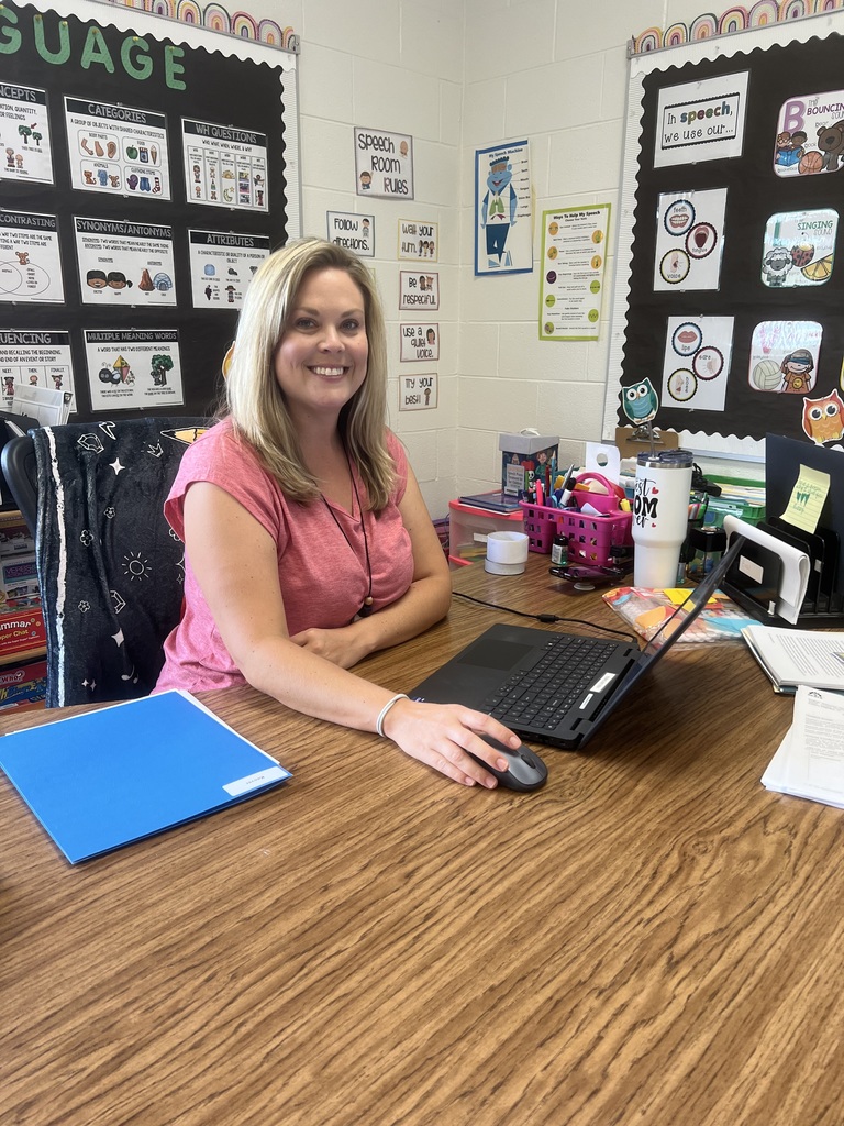 Teacher smiling at the camera, working on a computer