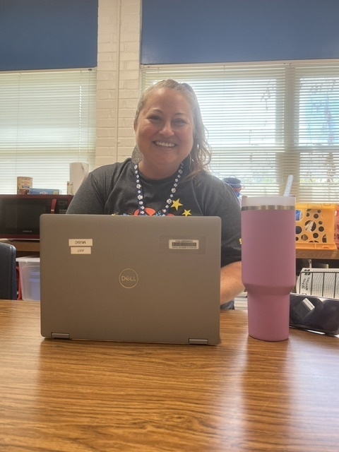 Teacher smiling at the camera, working on a computer