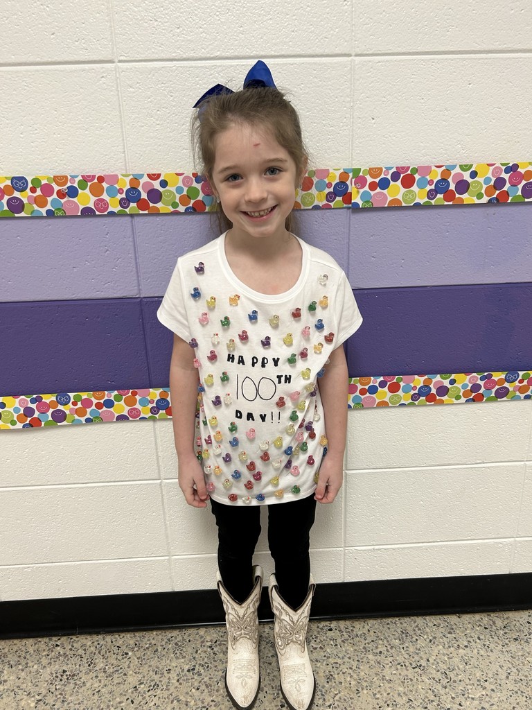 A student wearing a 100th day shirt decorated with 100 miniature ducks.