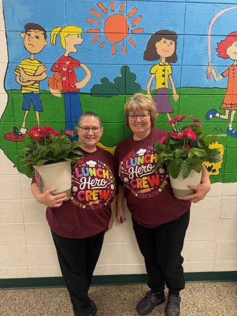 Ms. Alice Davis and Ms. Donna Underwood holding flowers wearing School Lunch Hero shirts.