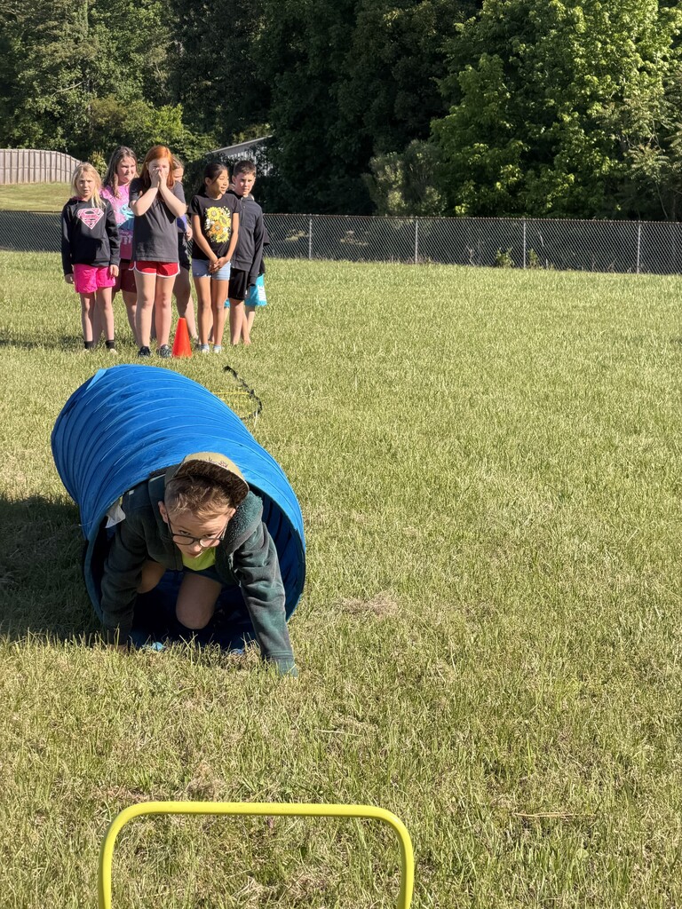 A student emerging from a tunnel while his classmates look on.