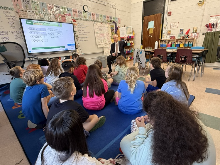 4th grade classroom listening to the superintendent reading a book. 
