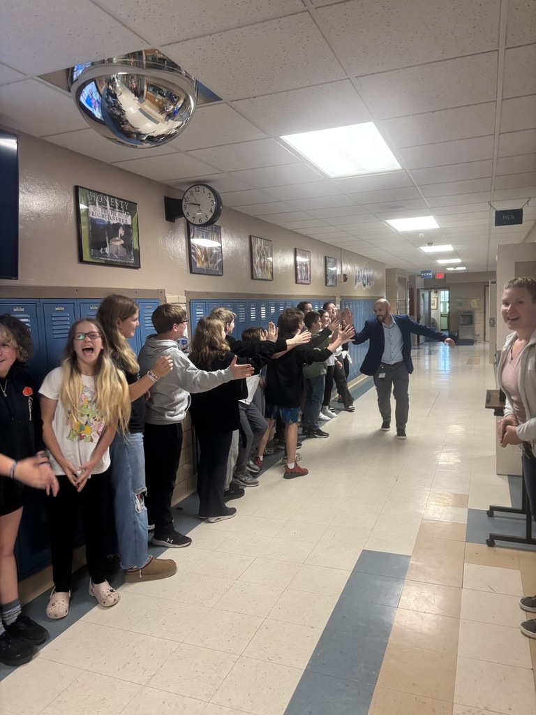students lined up in single file, all smiling and laughing, as the assistant principal runs down the line giving high fives.