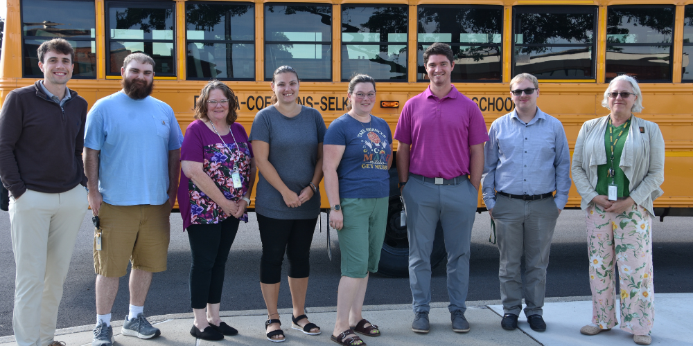 New teachers pose in front of a school bus in front of high school