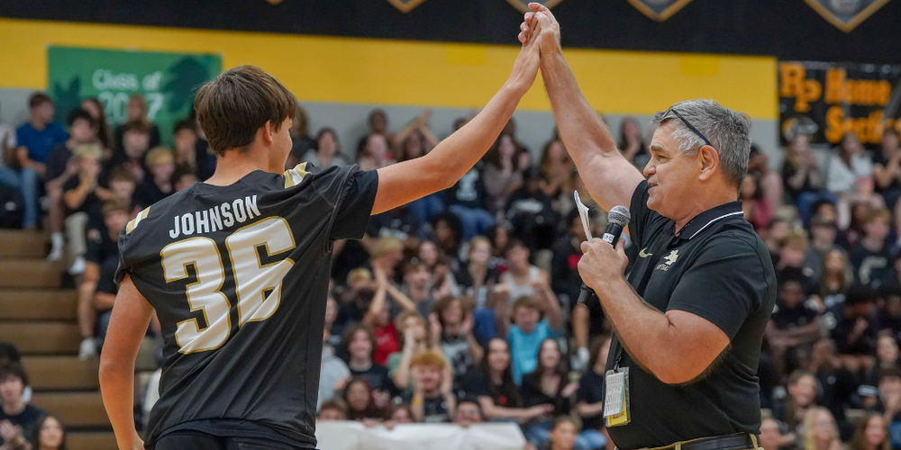 A student in a jersey and a teacher high five each other in a crowded gym