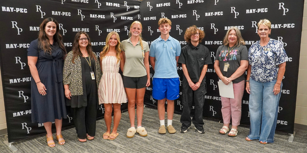 Four students stand between three teachers and a board member, smiling..