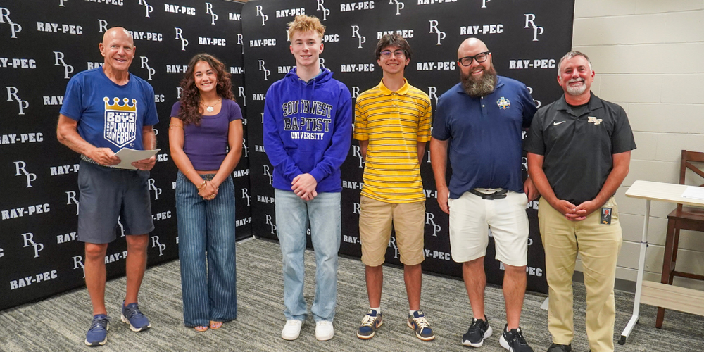 Five men and one girl stand in front of a Ray-Pec branded backdrop