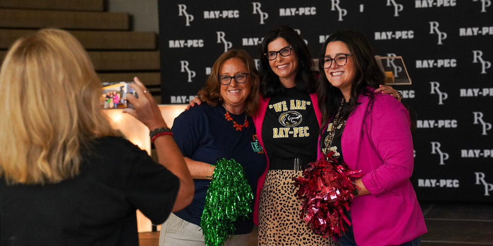 Three women smiling and posing for a photo in front of a backdrop with text "Ray Pec".