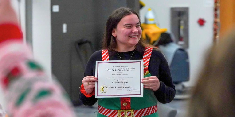 A girl stands smiling while holding up a certificate.
