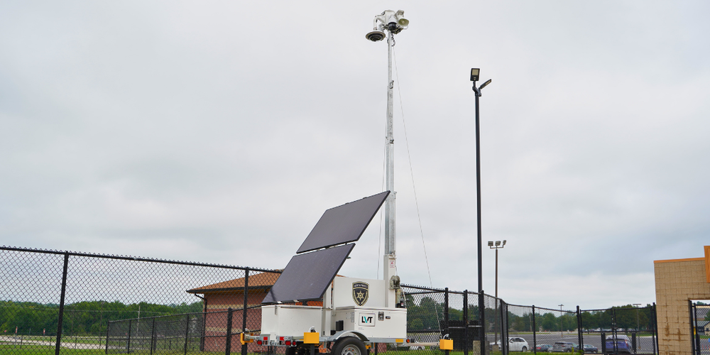 A security camera and siren sit near a fence in a stadium