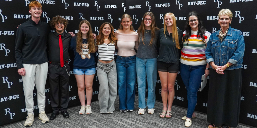 A group of teens and two women stand together smiling in front of a black backdrop with RP branding.