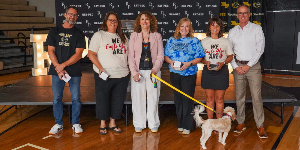 Six people standing together in front of a stage and one person has a dog on a leash.