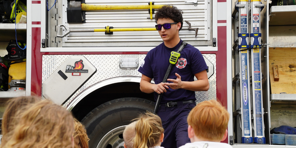 A firefighter stands in front of his truck while talking to a group of young students