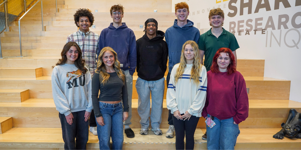 A group of students standing on a staircase. The girls are standing in front and the boys and standing behind the girls.