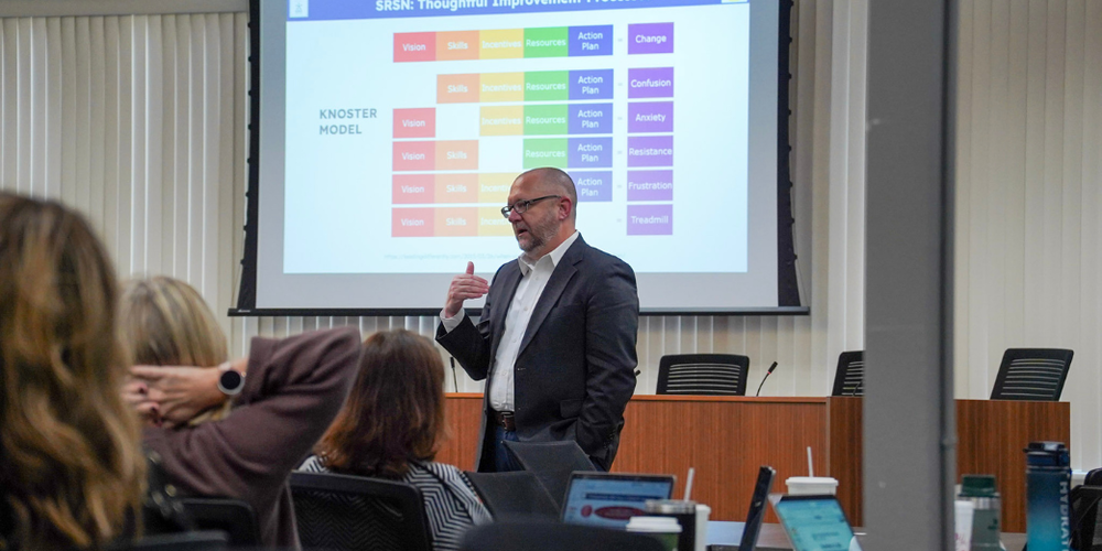 A man in a suit gives a presentation in a conference room full of people.