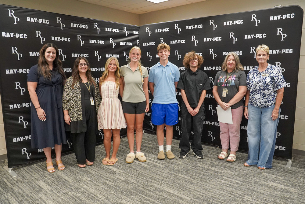Four students stand between three teachers and a board member, smiling..