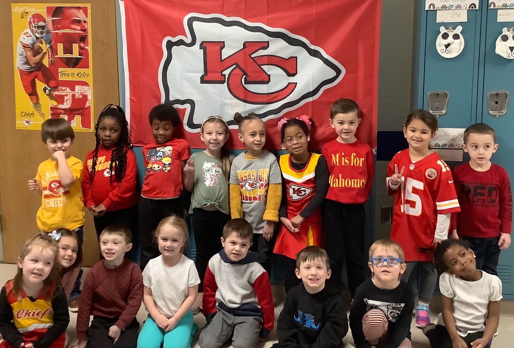 Children dressed in KC Chiefs spirit wear in front of a Chiefs flag.