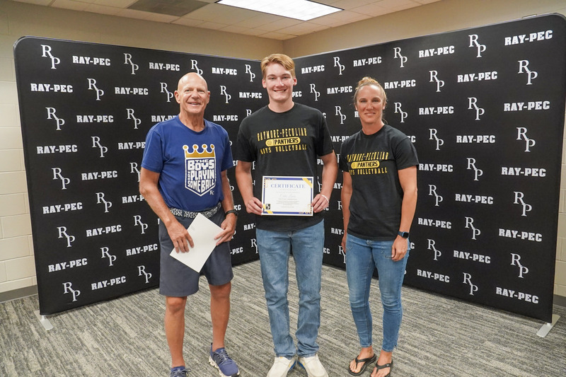 Three people stand together in front of a Ray-Pec branded backdrop