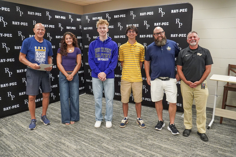 A group of boys and one girl stand together in front of a Ray-Pec branded backdrop.