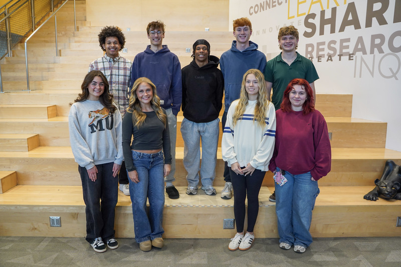 A group of students standing on a staircase. The girls are standing in front and the boys and standing behind the girls.