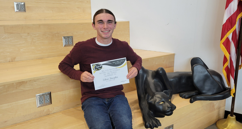 A student holding a certificate, sitting on a stair case with a panther statue next to them.