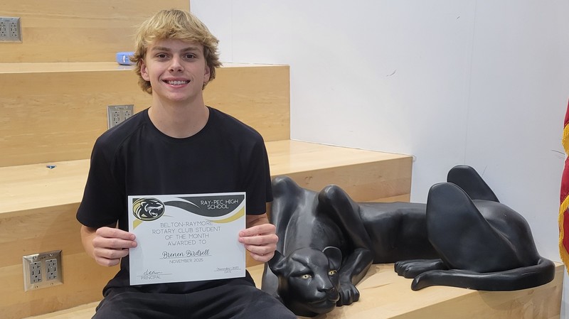 A student holding a certificate, sitting on a stair case with a panther statue next to them.