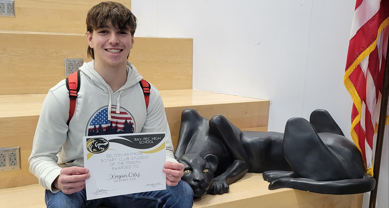 A student holding a certificate, sitting on a stair case with a panther statue next to them.
