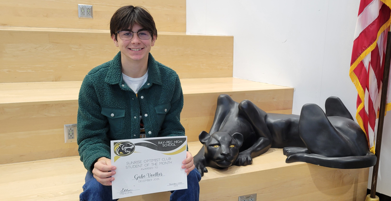 A student holding a certificate, sitting on a stair case with a panther statue next to them.
