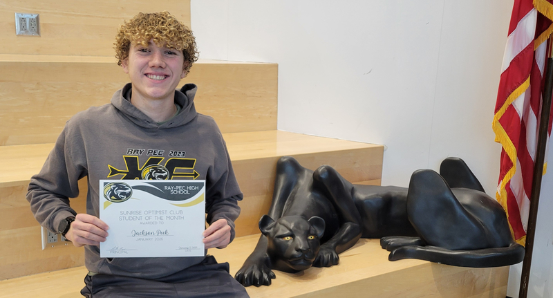 A student holding a certificate, sitting on a stair case with a panther statue next to them.