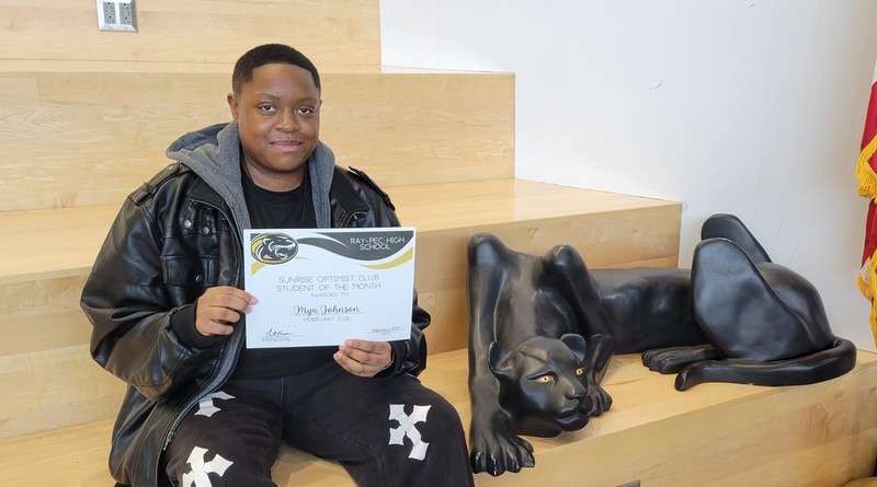 Student wearing black jacket and pants holding certificate for Student of the month posing with panther on a set of stairs.