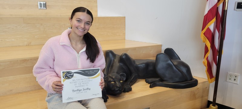 Student wearing pink sweatshirt holding certificate for Student of the month posing with panther on a set of stairs.