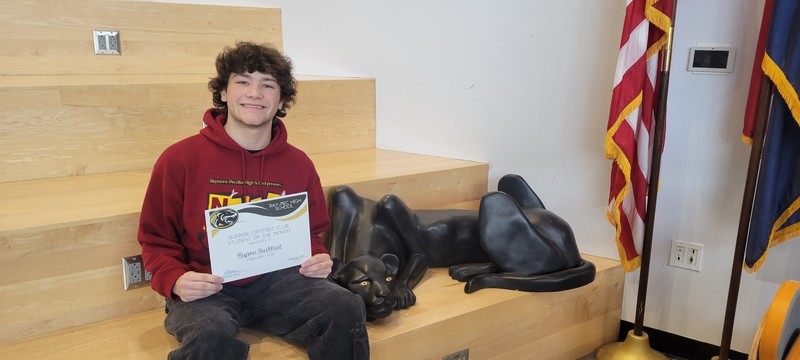 Student wearing red sweatshirt holding certificate for Student of the month posing with panther on a set of stairs.