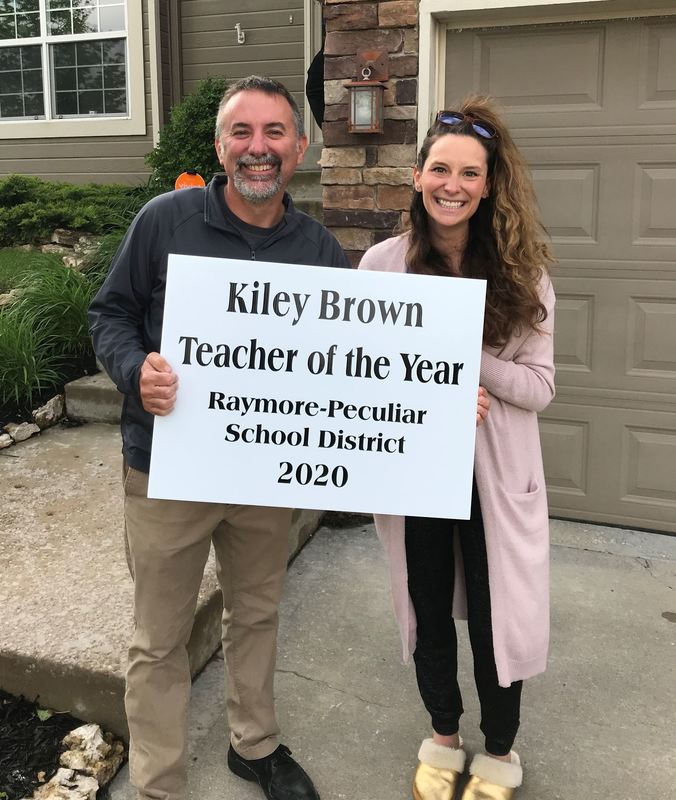 A man and a woman holding a sign that says "Kiley Brown Teacher of the Year 2020"