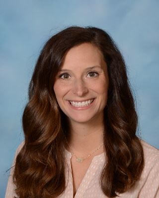 A lady with brown hair and a pink shirt smiling