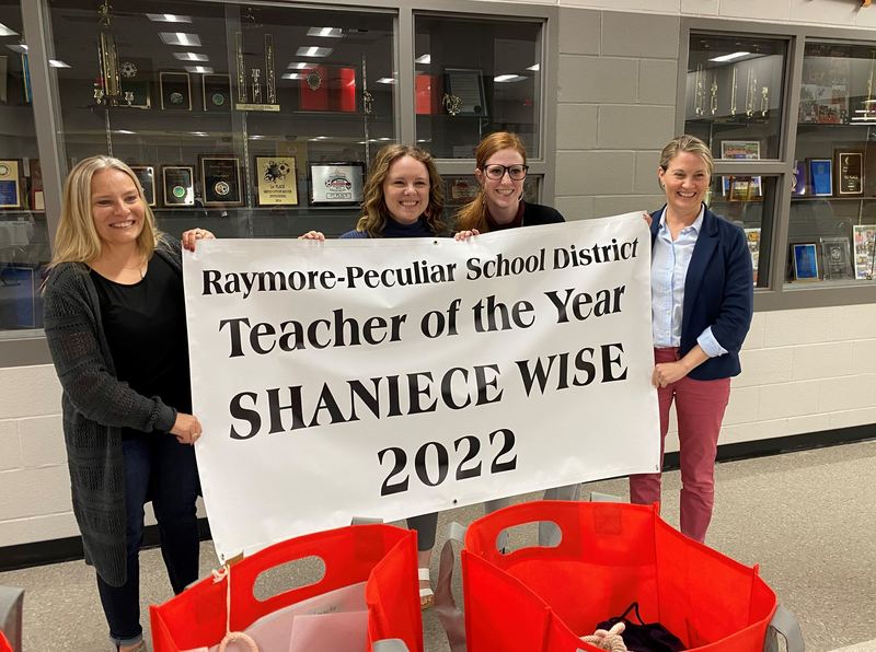 Four women stand together holding a big white banner