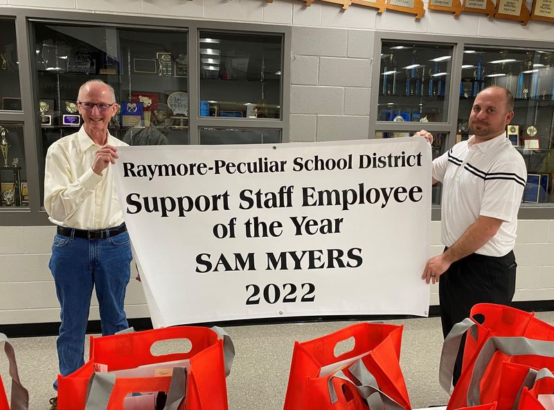 Two men stand opposite of each other holding a big white sign.