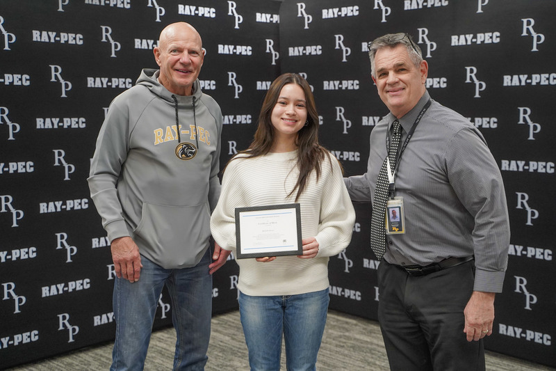 Two men and a woman stand together smiling. The woman is holding a certificate