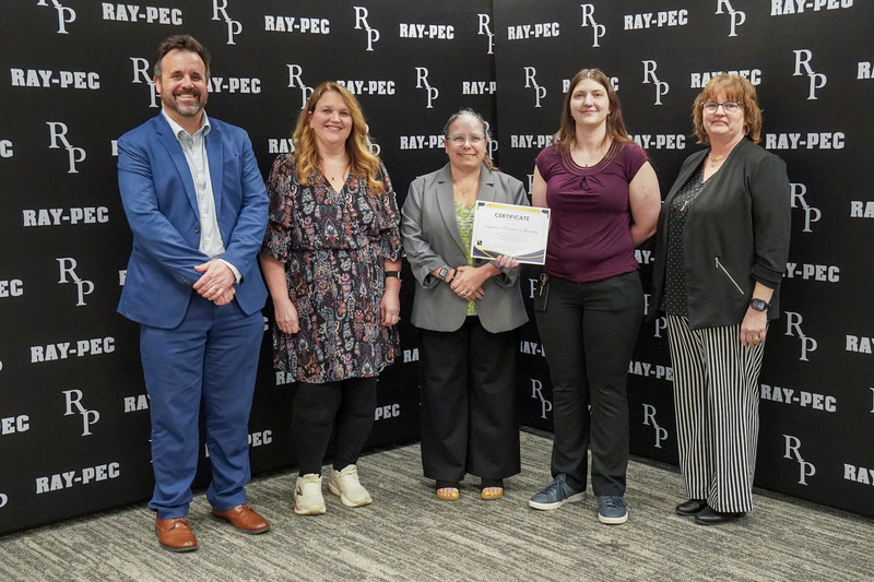 A group of women and one man stand in front of a black backdrop smiling