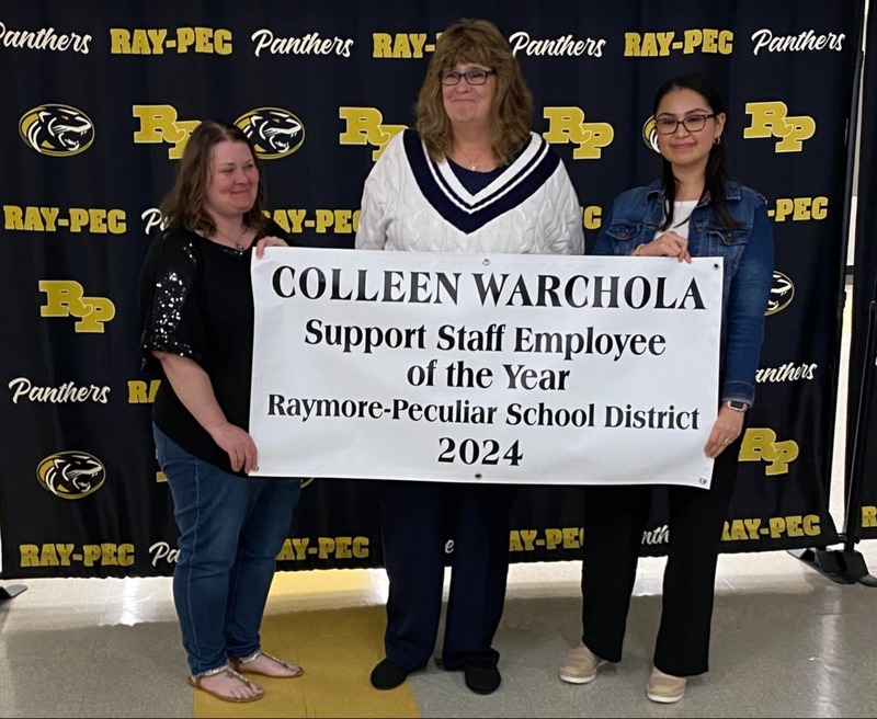 Three women stand together holding a banner that reads, "Collen Warchola Support Staff Employee of the Year 2024"