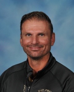 A man with a black shirt smiling in front of a blue backdrop