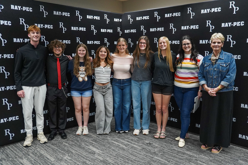 A group of young teens standing together smiling in front of a black backdrop with RP branding.