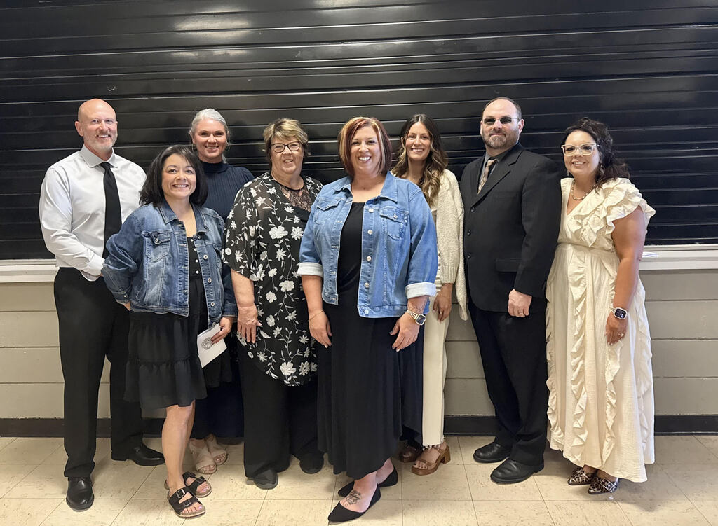 Group photo of the RE-1 Valley School District Board of Education and Superintendent standing indoors in front of a black wall panel. Seven adults are arranged in two staggered rows, smiling at the camera and dressed in professional and semi-formal attire. The photo appears on the district’s “Meet the Board” webpage above individual board member contact information.