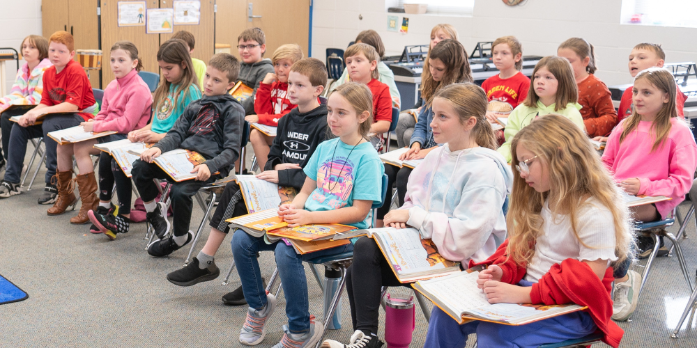 class full of students sitting with books on laps