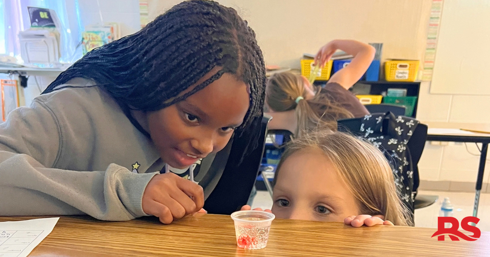 Two elementary students looking at a gummy bear submerged in a liquid.